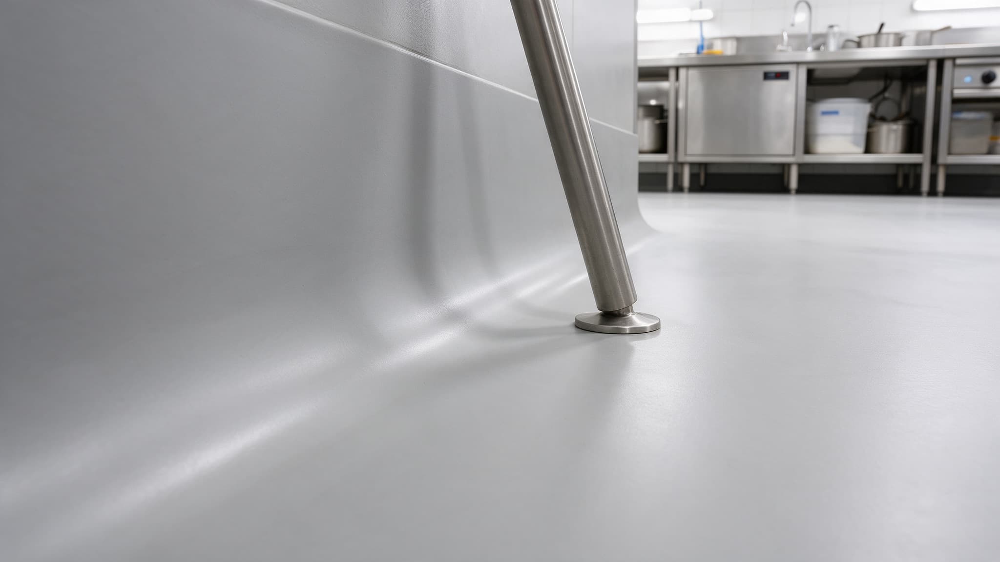 Coved resin base curving continuously from a commercial kitchen floor up the wall with no gap at the juncture